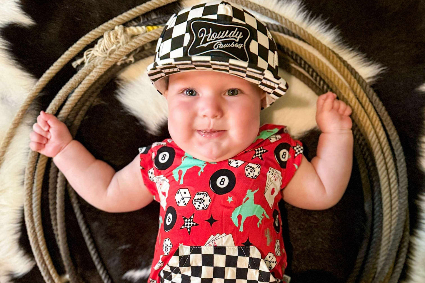Baby wearing a red patterned onesie and checkered hat on a rustic background